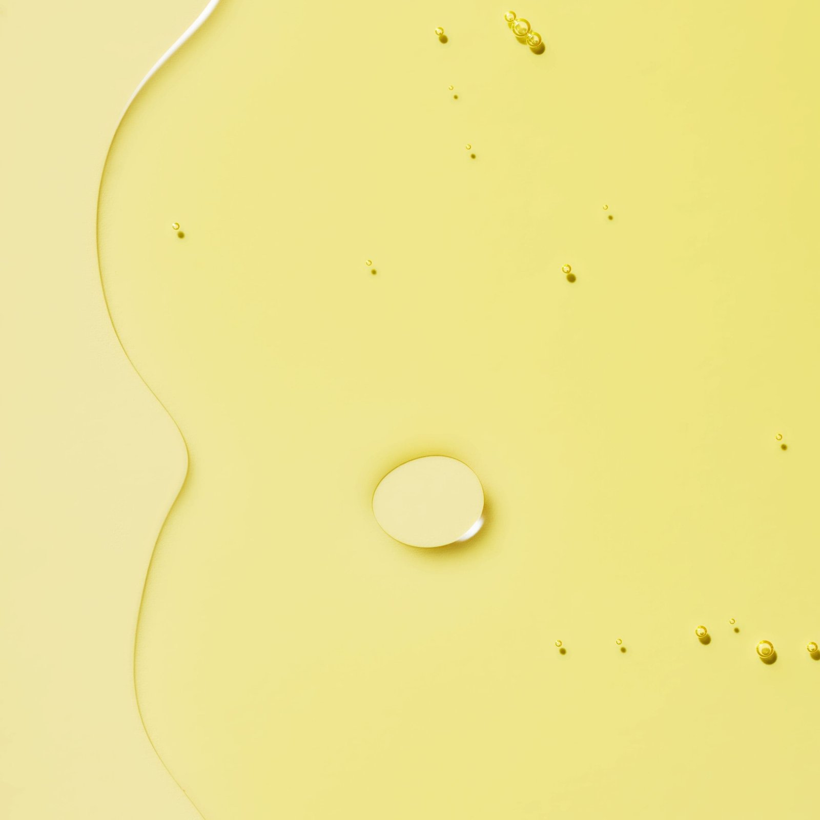 A smooth oil with droplets dispersed on a yellow background.