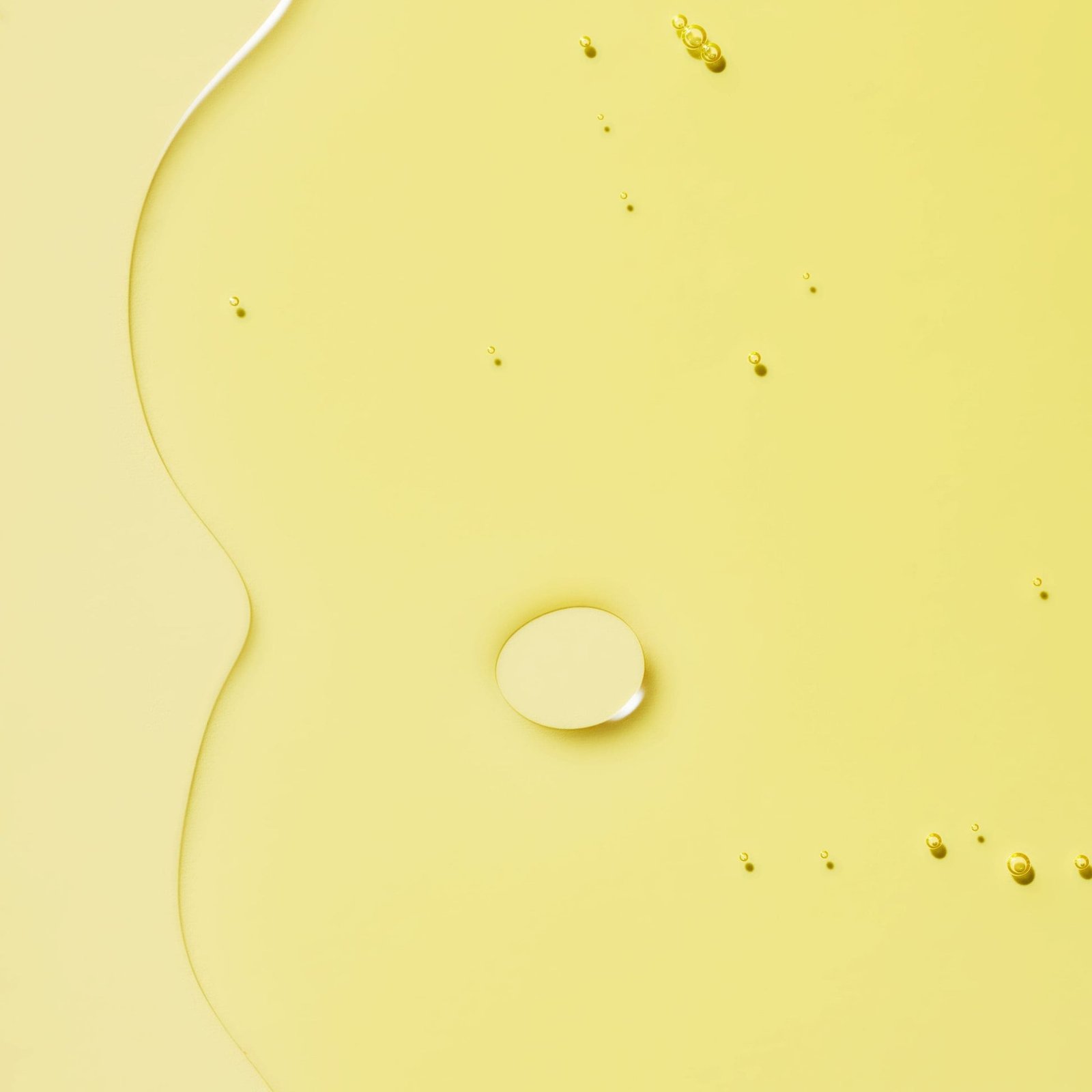 A smooth oil with droplets dispersed on a yellow background.