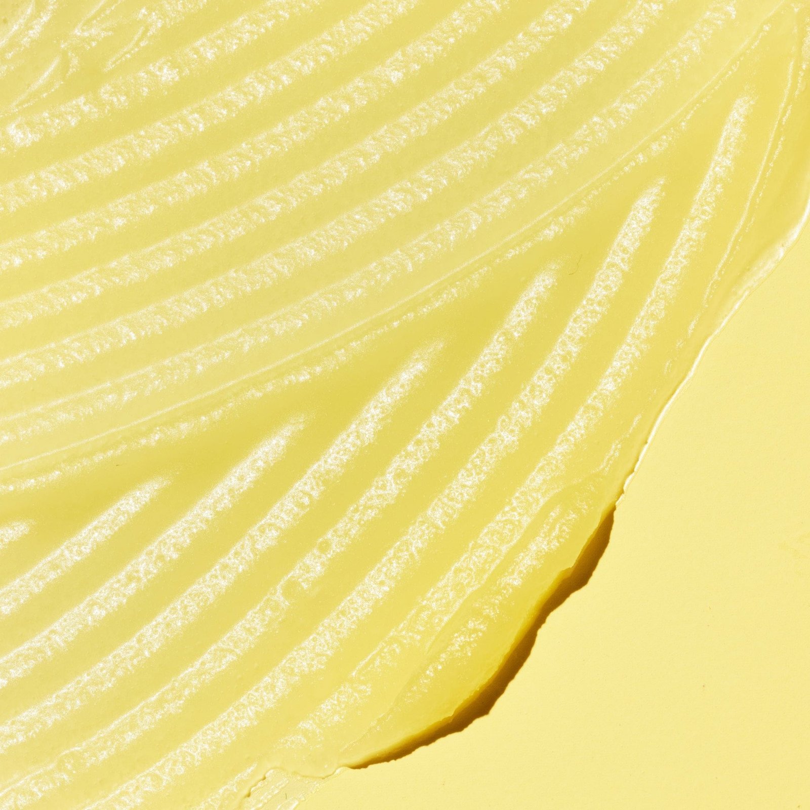 A close-up of a yellow gel-like texture with visible ridges, set against a yellow background.