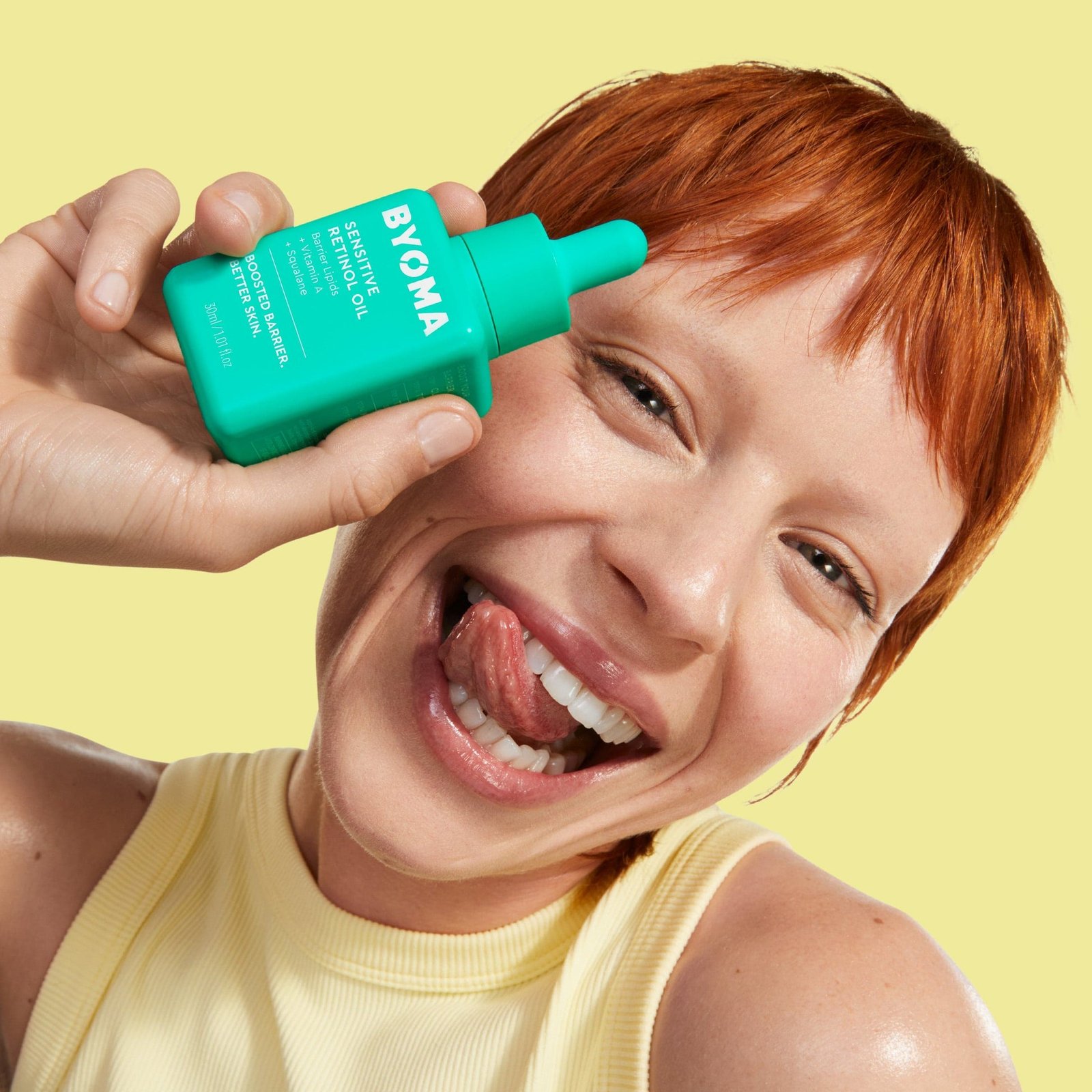 A person smiling and holding a bottle of Byoma Sensitive Retinol Oil.