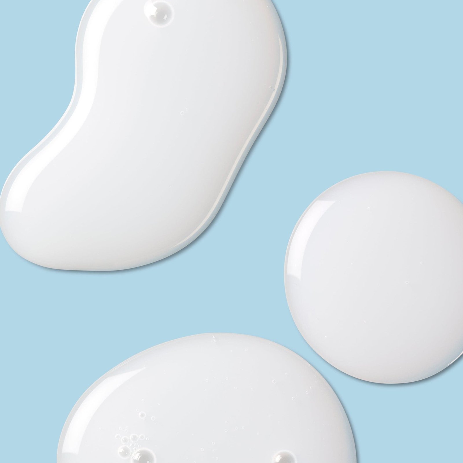 Smooth, glossy drops of white cream or lotion on a soft blue background.
