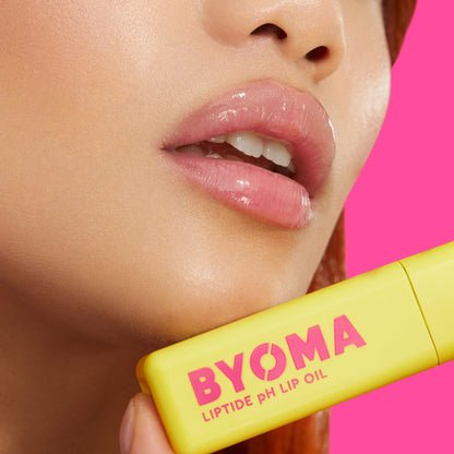 A model with glossy lips holds BYOMA Liptide pH Lip Oil to their chin.