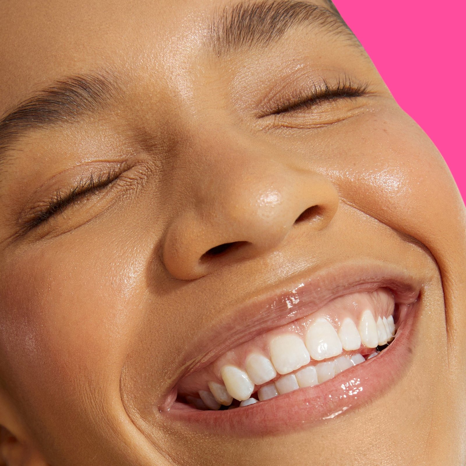 A smiling model with radiant, dewy skin and glossy lips.