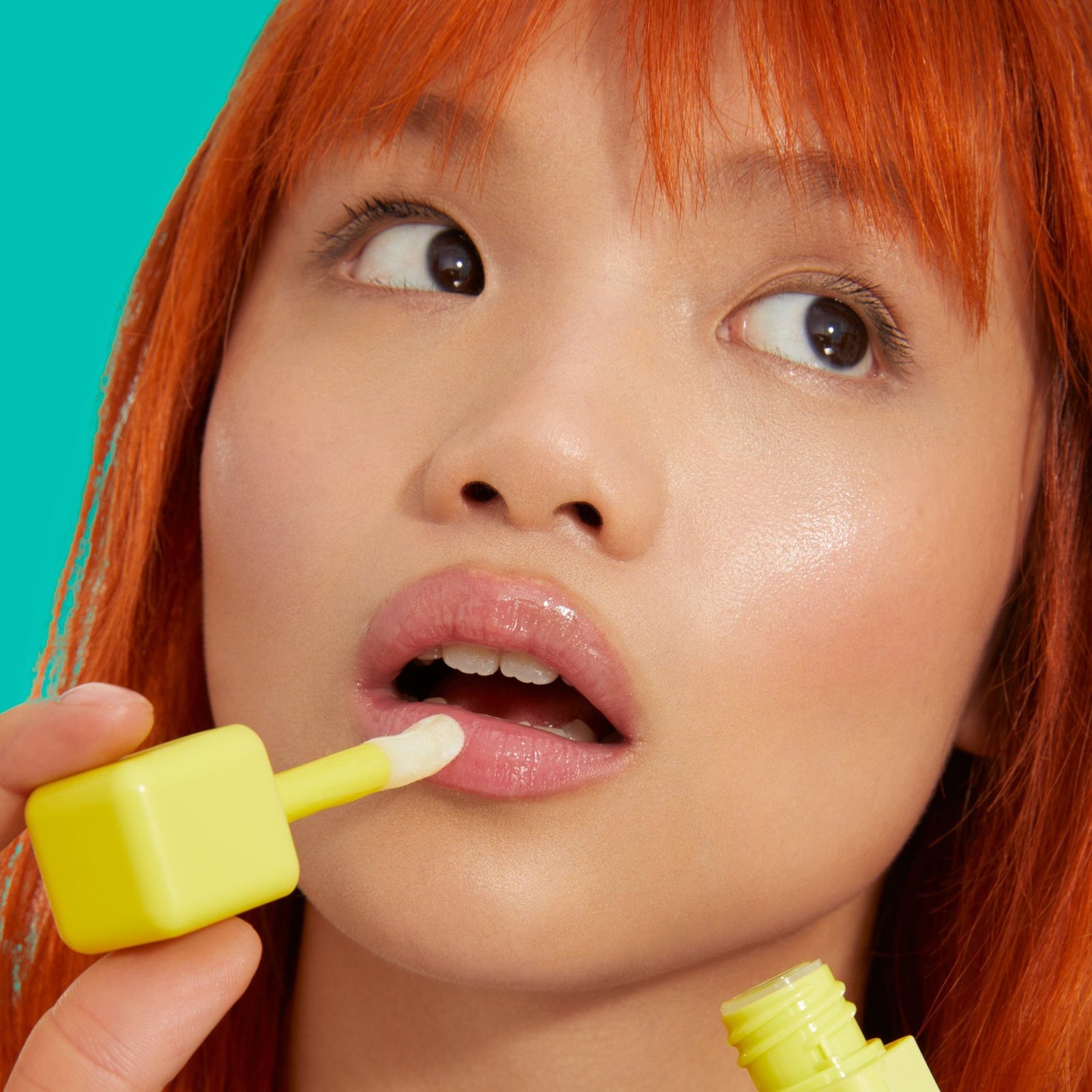 A woman with vibrant red hair applying BYOMA Liptide Lip Oil with a plush applicator.