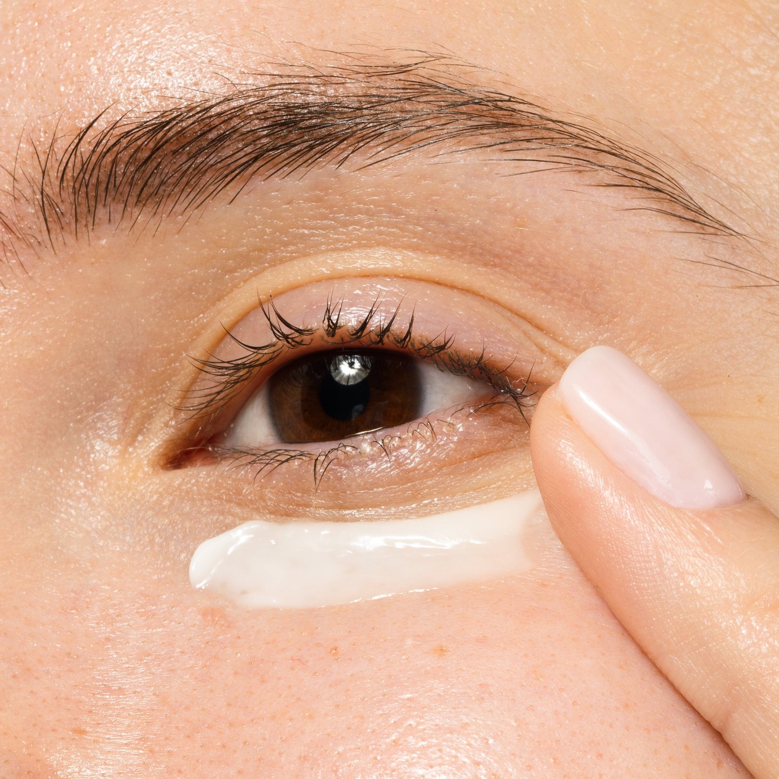 A person applying eye cream under their eye with their finger.