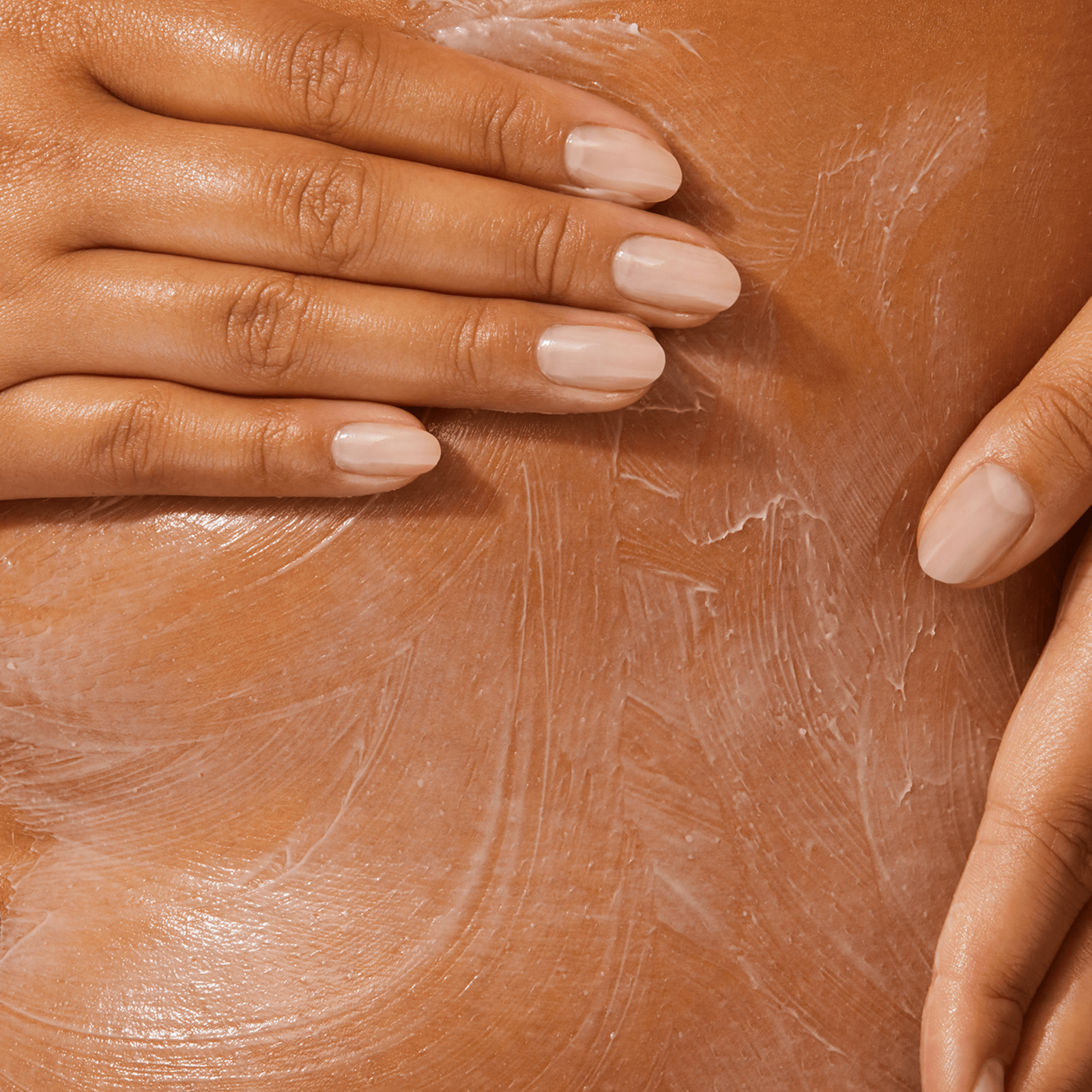 A close-up of a person’s torso, with two hands gently applying body cream.