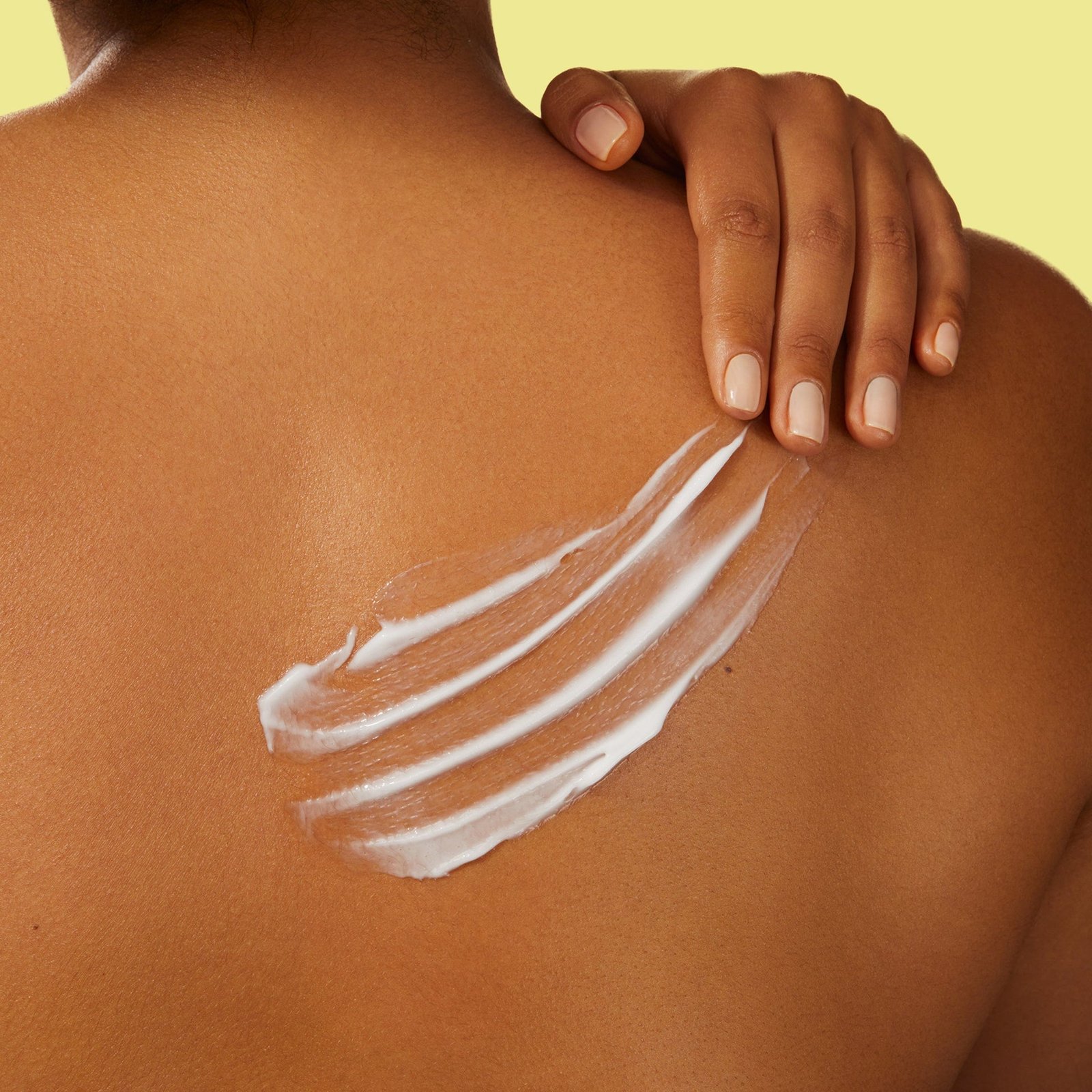 A person applies a body lotion to their shoulder. 