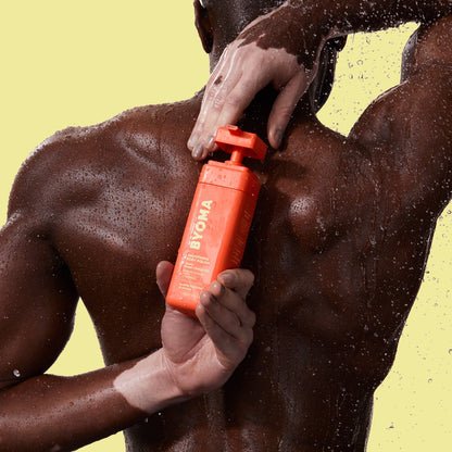 A man holding Byoma Body Polish behind his upper back.