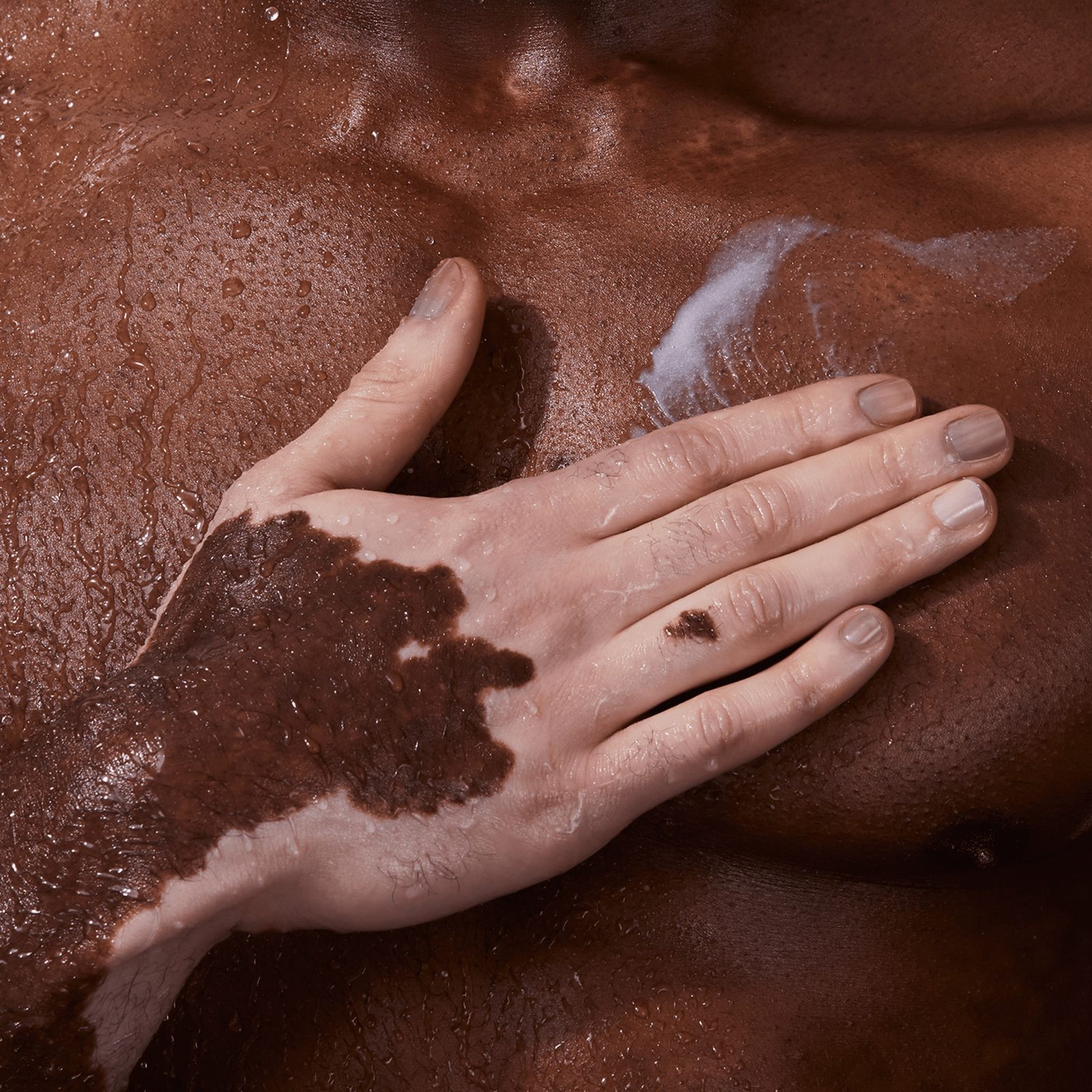 A close-up of a person’s chest with body wash being applied by a hand.