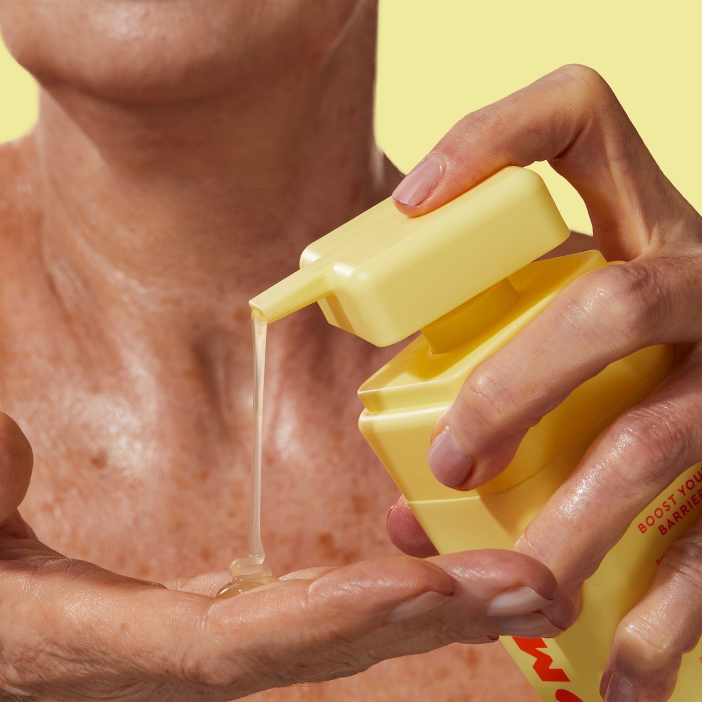 A person with mature skin is dispensing a translucent liquid onto their hand.
