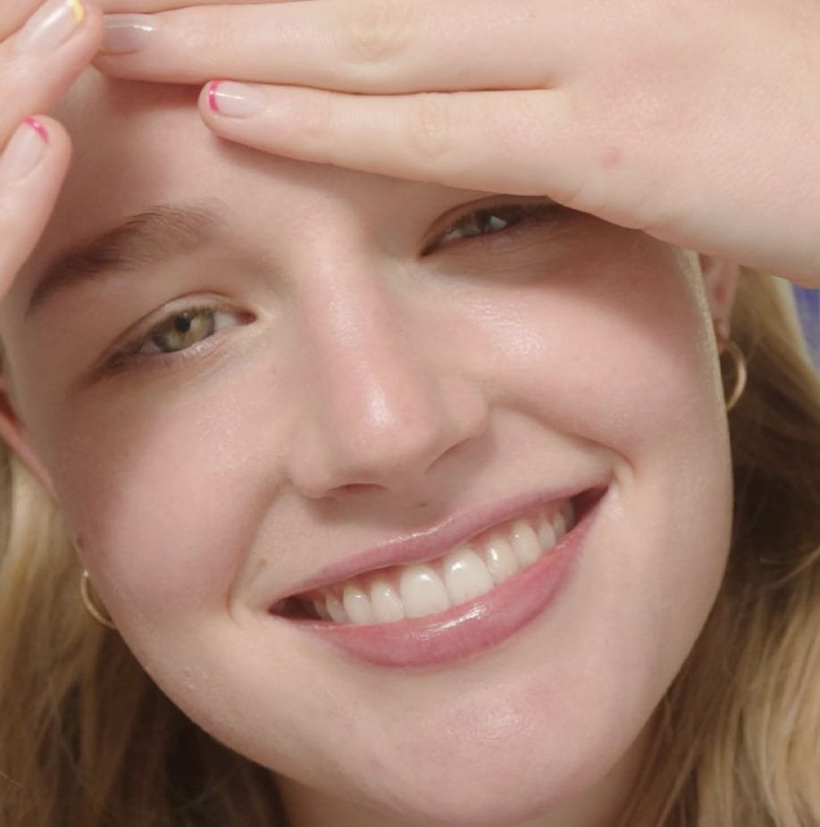 A smiling woman with glowing skin, gently touching her forehead, highlighting hydration and radiance.