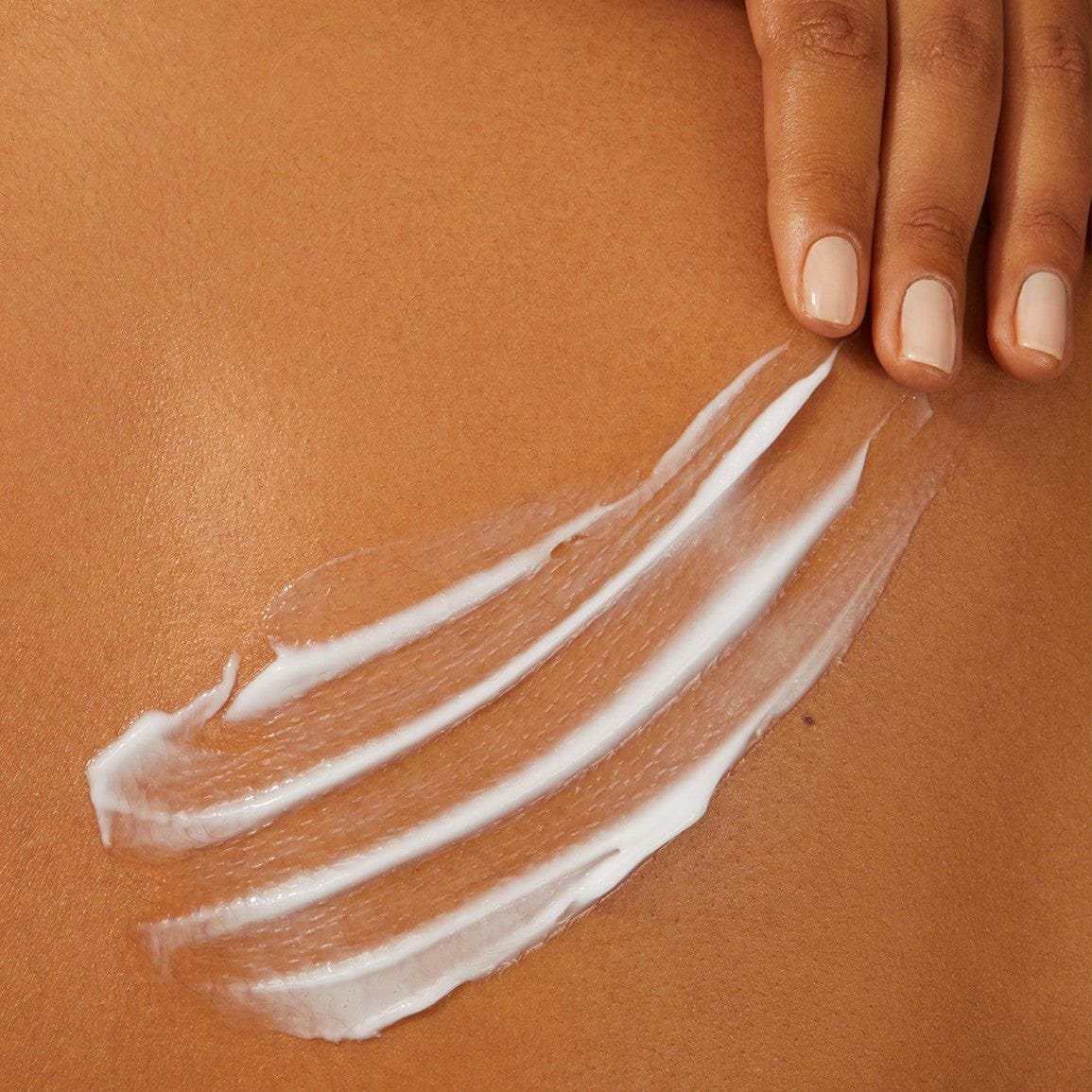 Hand spreading white lotion on smooth skin.