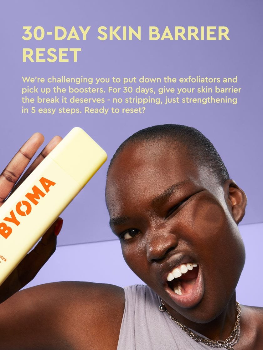 A smiling woman with dark skin and short hair, whose face is pressed against an invisible barrier, holds a yellow BYOMA product labeled "Creamy Jelly Cleanser." Text on the left side reads "30-DAY SKIN BARRIER RESET" and explains a 30-day challenge to avoid exfoliators and use barrier-boosting skincare. Background is lavender-purple.
