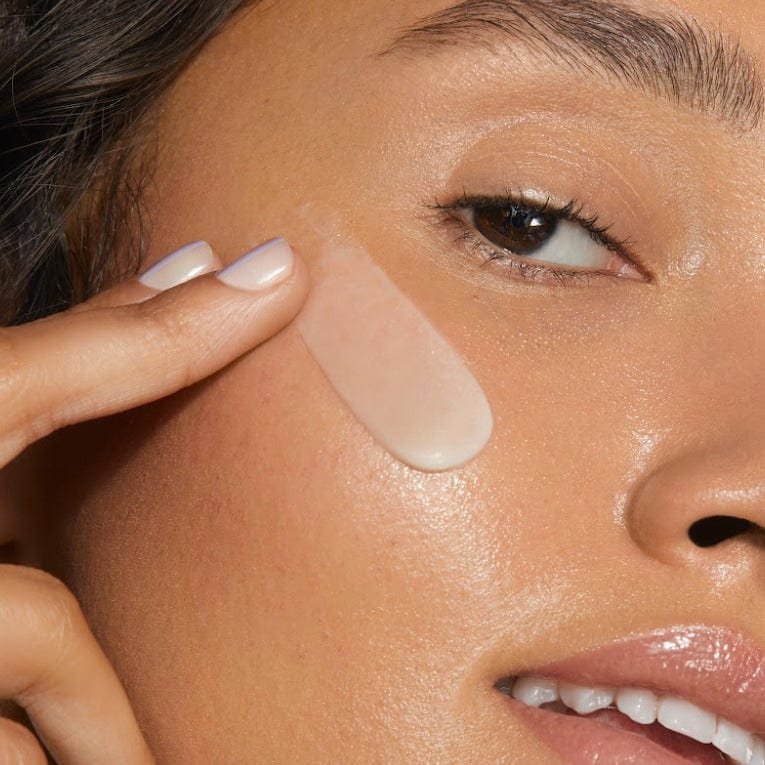 Close-up of a woman applying a creamy skincare product to her cheek.